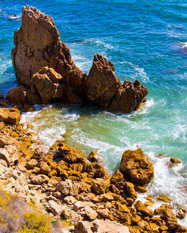 A large, jagged rock juts out of the ocean floor on the coast of the Pacific Ocean in Southern California.